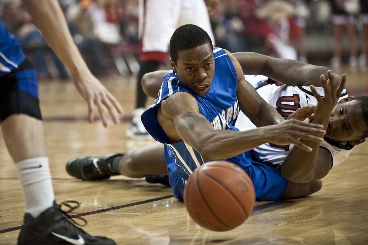 joueurs de basket se disputant le gain du ballon au sol avec hargne