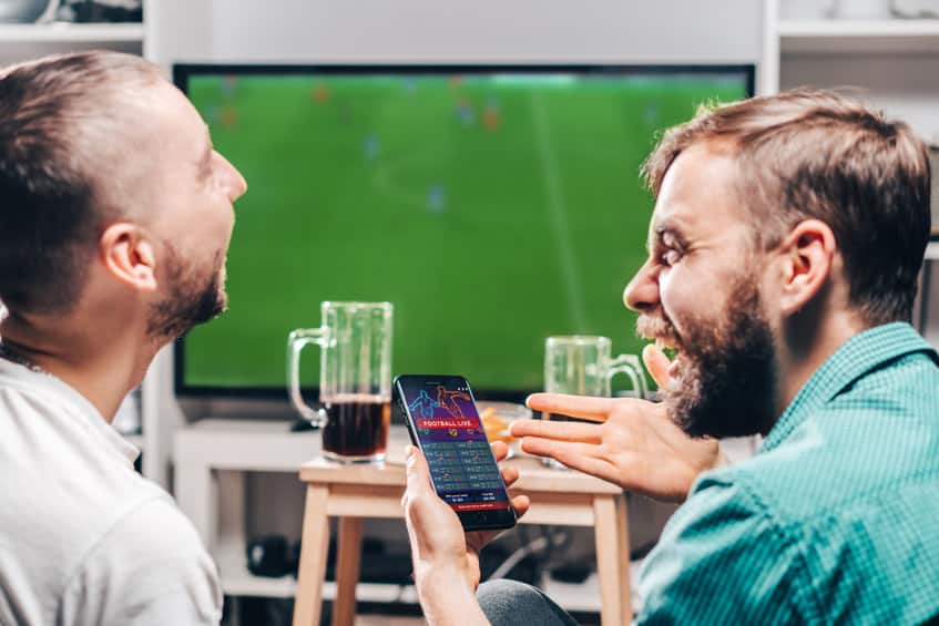 deux amis regardent un match de football à la tv en pariant sur leur smartphone