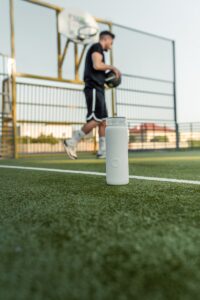 Un joueur de basket s'entraine au basketball avec une bouteille d'eau disposée sur le sol à proximité